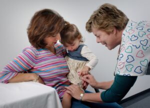A parent measures liquid medicine with a dosing syringe for a young child sitting at a kitchen table.